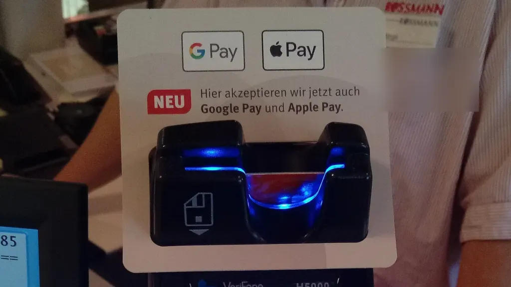Platobný terminál pri pokladni s nálepkou s logami Google Pay a Apple Pay nad čítačkou kariet