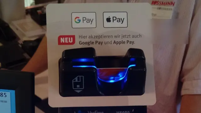 Platobný terminál pri pokladni s nálepkou s logami Google Pay a Apple Pay nad čítačkou kariet
