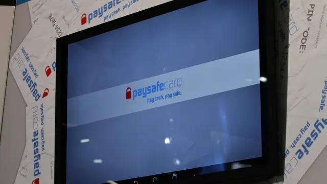 Logo paysafecard na obrazovke výstavného stánku obklopenej dekoráciou v tvare poukážok paysafecard